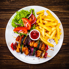 Kebabs - grilled meat with french fries and vegetables on wooden background