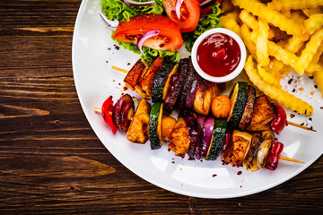 Kebabs - grilled meat with french fries and vegetables on wooden background