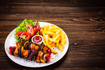 Kebabs - grilled meat with french fries and vegetables on wooden background
