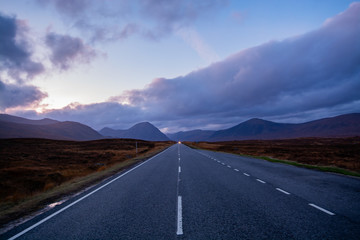 Straight motorway/highway with mountains and sun setting in far distance
