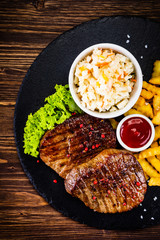 Grilled steak with french fries and vegetables served on black stone on wooden table
