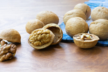 Whole walnuts and walnut kernel halves without shell on a dark wooden table and checkered towel, close up. Seeds of the common walnut tree Juglans regia. Macro food photo close up view.