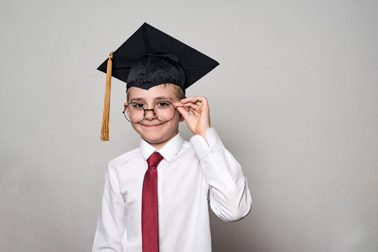 Boy in a square academic cap and white shirt correcting glasses. White background. School concept