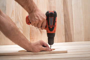 Electric drill screwdriver in male hand. Tightening screw, processing workpiece on light brown...