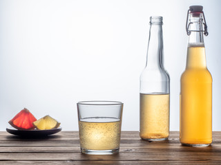 Two bottles and glass of kombucha drink on a wooden table with a slice of lemon and a slice of grapefruit on the plate.