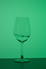 Wine glass on a long stem. A little drink is poured into it, a splash is visible. In back green.