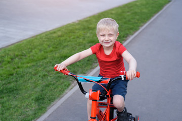Fototapeta na wymiar Portrait of a handsome blond boy rides on a children's bicycle. Urban background