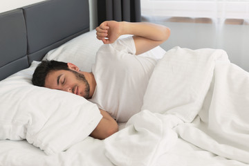 Young handsome man sleeping in his bed. The man is yawning and stretching.