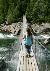 Middle aged woman walking over a suspension bridge in summer