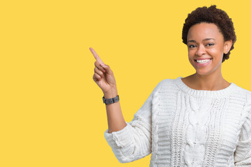 Beautiful young african american woman wearing sweater over isolated background with a big smile on face, pointing with hand and finger to the side looking at the camera.