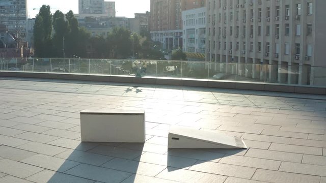 Aerial view of skateboarder jumping at speed on bank and sliding along curb against background of urban buildings in sunlight. Skillful male showing frontside 50-50 grind stunt skateboarding outdoors