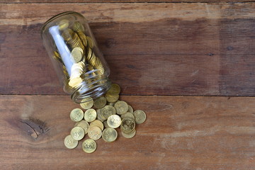 Side view of coins in glass bottle on wooden background
