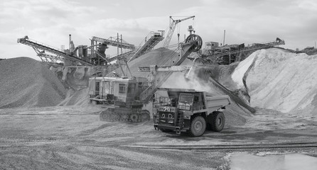 Heavy truck, excavator and rock stone crushing complex, black and white panorama. Mining industry. Quarry and mining equipment.