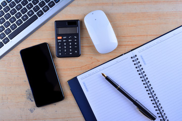 The keyboard with mouse, fountain pen, notebook, calculator and smartphone on a table