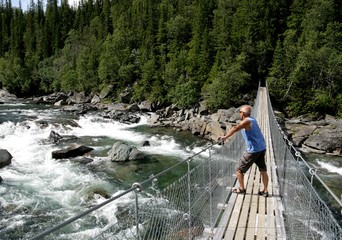 Man on a suspension bridge looking at a waterfall
