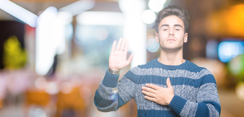Young handsome man over isolated background Swearing with hand on chest and open palm, making a...