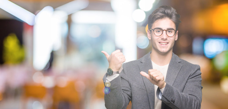 Young business man wearing glasses over isolated background Pointing to the back behind with hand and thumbs up, smiling confident