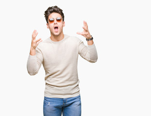 Fototapeta premium Young handsome man wearing sunglasses over isolated background crazy and mad shouting and yelling with aggressive expression and arms raised. Frustration concept.