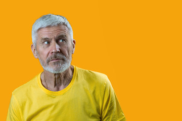 portrait of surprised and curious gray-haired man with a beard on a yellow background