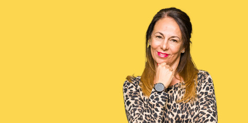 Beautiful middle age woman wearing leopard animal print dress looking confident at the camera with smile with crossed arms and hand raised on chin. Thinking positive.