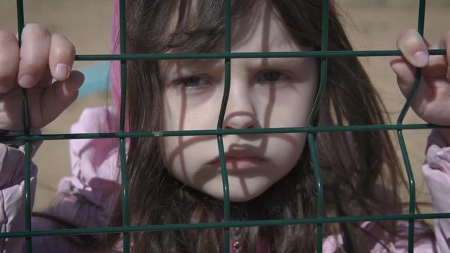 Behind grid. A child in a refugee camp. Sad little girl behind an iron bars.