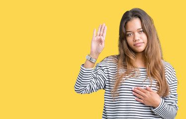 Young beautiful brunette woman wearing stripes sweater over isolated background Swearing with hand on chest and open palm, making a loyalty promise oath