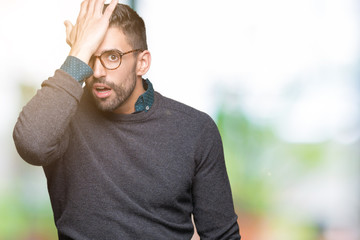 Young handsome man wearing glasses over isolated background surprised with hand on head for...