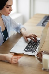 Smiling woman online shopping using computer and credit card in kitchen