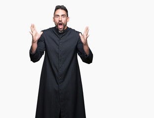 Fototapeta premium Young Christian priest over isolated background celebrating crazy and amazed for success with arms raised and open eyes screaming excited. Winner concept