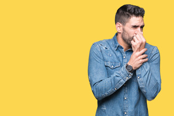Young handsome man over isolated background smelling something stinky and disgusting, intolerable...