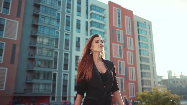 Gorgeous young woman going to work, passing modern buildings. Portrait of successful happy business woman on her way to work on street. Female portrait, low angle shot, slow motion