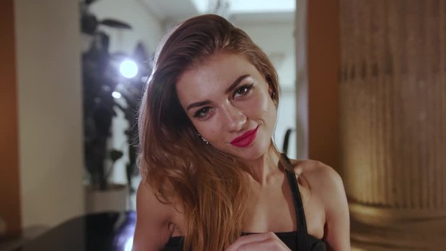 Hot young woman with sexy pink lips and natural makeup and trendy black dress provocatively looking straight to camera. Hot, seduction, romantic mood. Female portrait, close up view