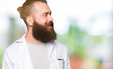 Young blond scientist man wearing white coat looking away to side with smile on face, natural...