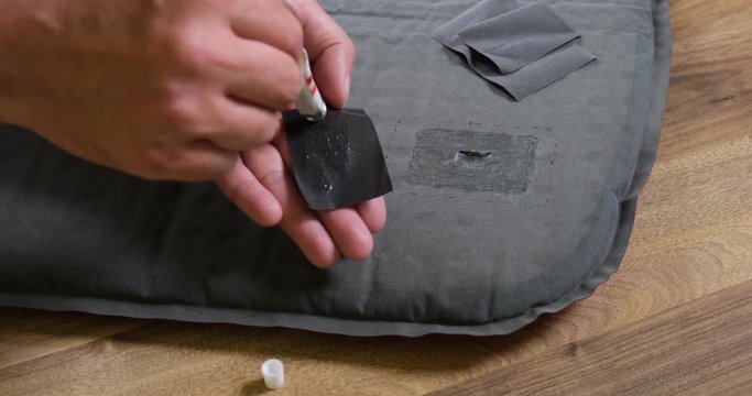 Close up of male hand applying glue on a repair patch for fixing a puncture in a tent sleeping pad. Self repairing camping gear.