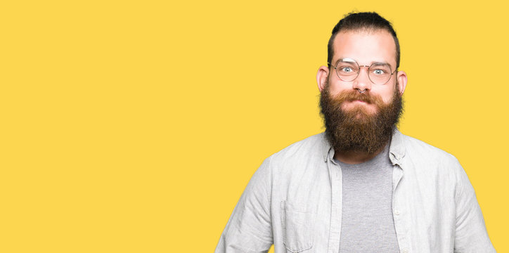 Young blond man wearing glasses puffing cheeks with funny face. Mouth inflated with air, crazy expression.