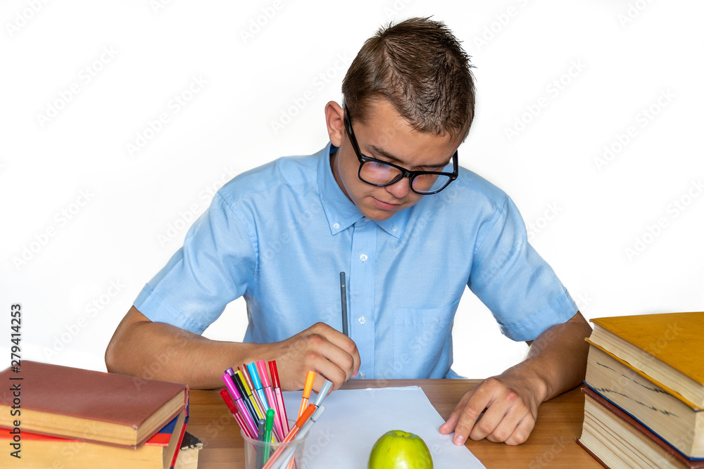 Wall mural joyful teen boy sitting at the table with pencils and textbooks. happy pupil doing homework at the t