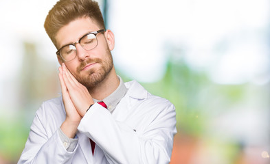 Young handsome scientist man wearing glasses sleeping tired dreaming and posing with hands together while smiling with closed eyes.