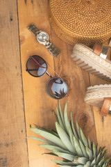 Summer background with a wicker fashionable bag, and women's summer shoes, tropical pineapple and sun glasses. Summer fashion, the concept of the holiday.Flat lay.On the old wooden background,vertical