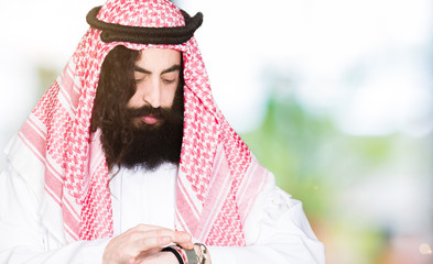 Arabian business man with long hair wearing traditional keffiyeh scarf Checking the time on wrist watch, relaxed and confident
