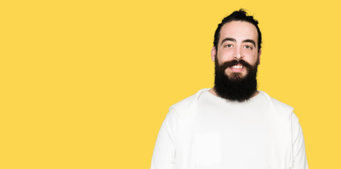 Young man with long hair and beard wearing sporty sweatshirt with a happy and cool smile on face. Lucky person.