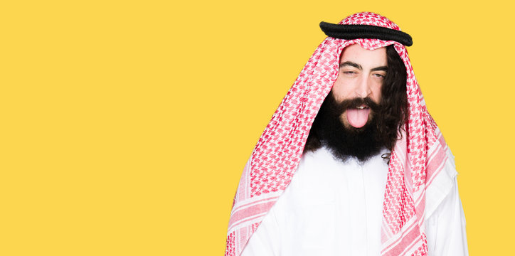 Arabian Business Man With Long Hair Wearing Traditional Keffiyeh Scarf Sticking Tongue Out Happy With Funny Expression. Emotion Concept.