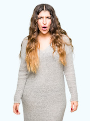 Young beautiful woman wearing winter dress afraid and shocked with surprise expression, fear and excited face.