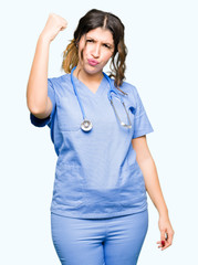 Young adult doctor woman wearing medical uniform angry and mad raising fist frustrated and furious while shouting with anger. Rage and aggressive concept.