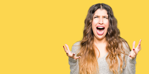 Young beautiful woman wearing winter dress crazy and mad shouting and yelling with aggressive expression and arms raised. Frustration concept.