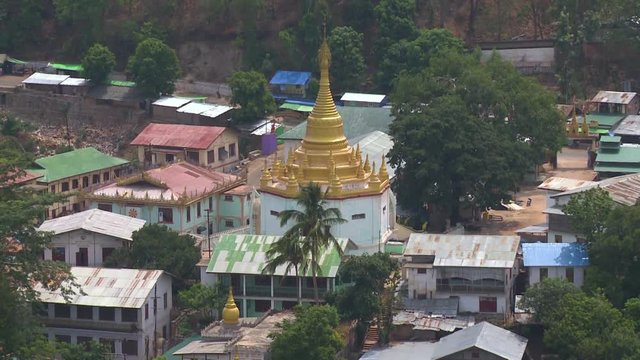 A birds eye view houses and some trees surrounding a temple painted in white with a golden roof