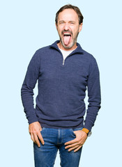 Fototapeta premium Middle age handsome man wearing a sweater sticking tongue out happy with funny expression. Emotion concept.
