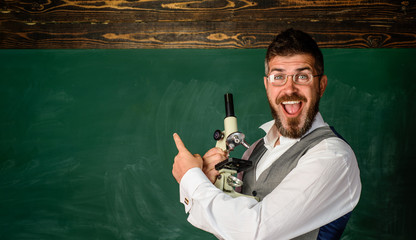 Smiling student in classroom. Scientist holds microscope. Teacher with microscope near chalkboard,...