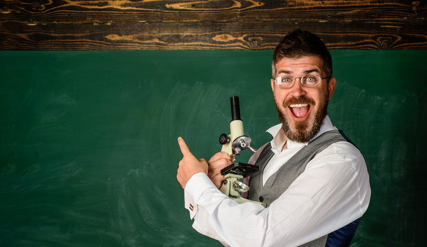 Smiling student in classroom. Scientist holds microscope. Teacher with microscope near chalkboard, copy space. Education, science. Scientifics research. Biology or chemistry lesson in university.