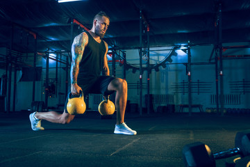 Young healthy man athlete doing exercise with the weights in the gym. Single male model training...