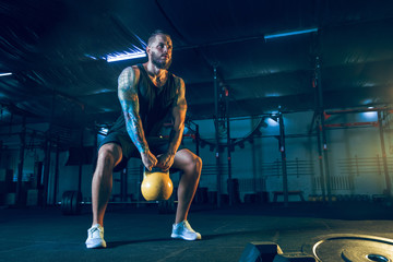 Young healthy man athlete doing exercise with the weights in the gym. Single male model training...